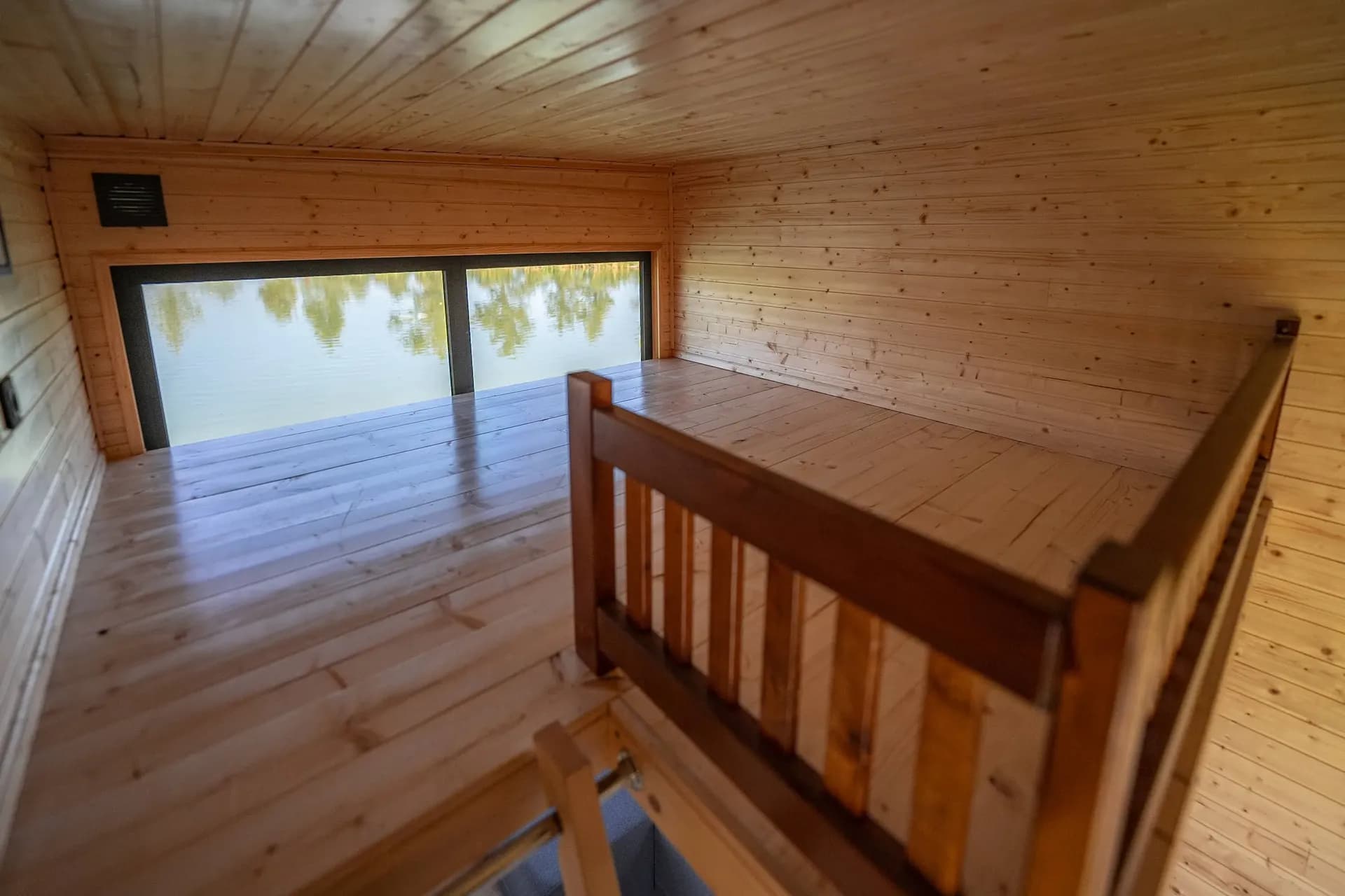 Séjour en bois clair, mezzanine et baie vitrée sur un lac