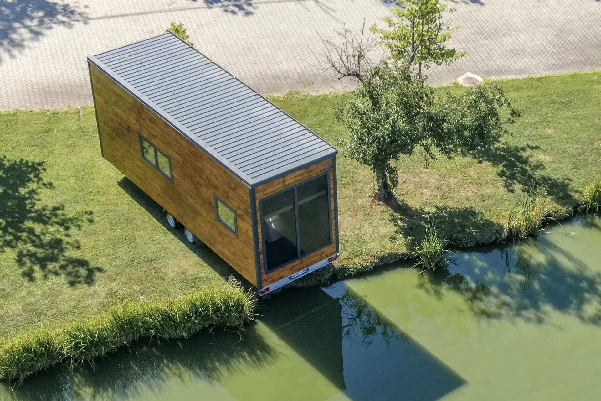 Tiny house en bois sur sa remorque, vue du dessus, au bord d’un étang